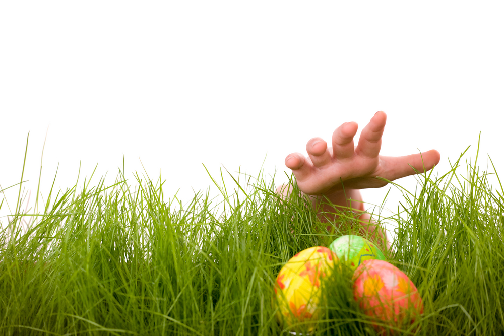Child’s hand reaches for easter eggs hidden in grass