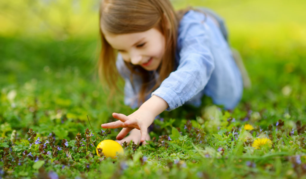 Little girl hunting for Easter eggs in a green field